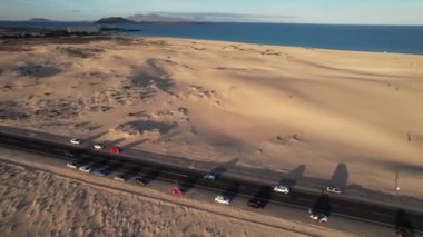 Fuerteventura 'daki kum tepeleri arasında giden arabanın hava görüntüsü.