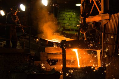 Metalürjist ocaktan sıcak erimiş metal döküyor.