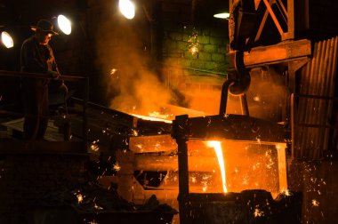 Metalürjist ocaktan sıcak erimiş metal döküyor.