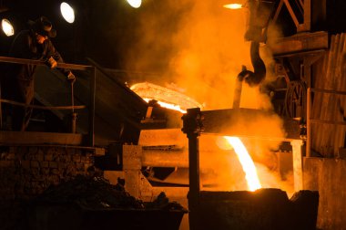 Metalürjist ocaktan sıcak erimiş metal döküyor.