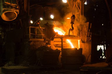 Metalürjist ocaktan sıcak erimiş metal döküyor.