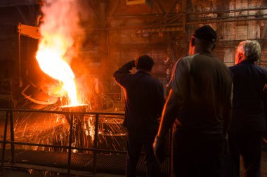 Metalürjistler erimiş metalin küfe dökülmesini izliyorlar.