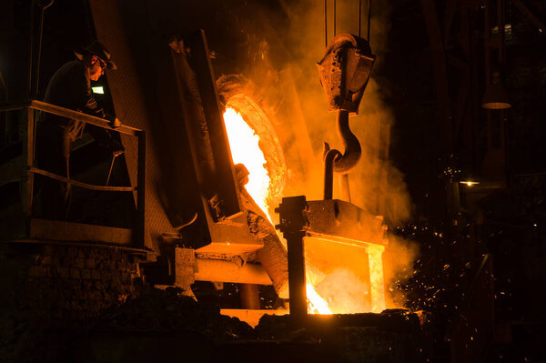 Metallurgist pouring hot molten metal out of furnace