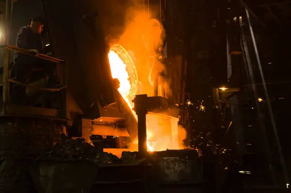 Metalürjist ocaktan sıcak erimiş metal döküyor.