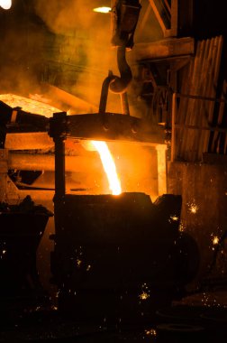 Metalürjist ocaktan sıcak erimiş metal döküyor.