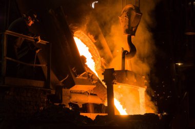 Metalürjist ocaktan sıcak erimiş metal döküyor.