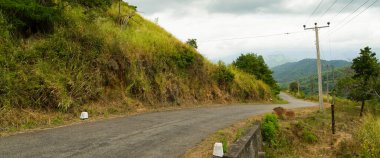 Bulutlu gökyüzü ile tepelik tropikal peyzaj boş dar yol