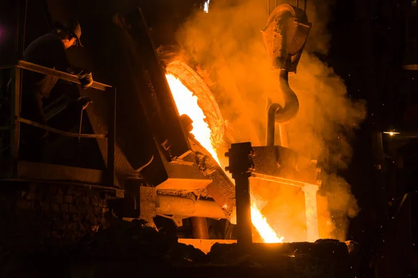 Metalürjist ocaktan sıcak erimiş metal döküyor.