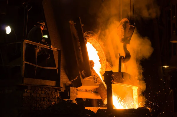 Metalürjist ocaktan sıcak erimiş metal döküyor.