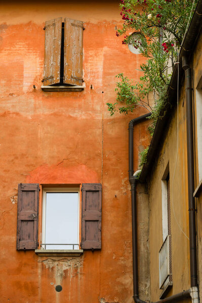 Red facade of hold house in Bologna city centre with wooden window shutters