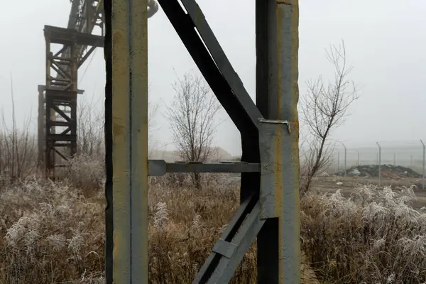Terk edilmiş bir sanayi bölgesinde kış sisi ve donuyla kaplı paslı metal yapı.