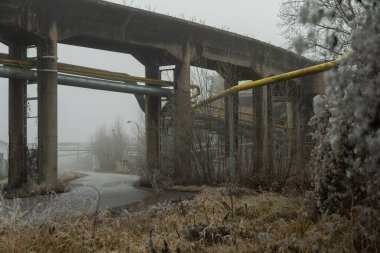 Kış sisinde terk edilmiş bir sanayi bölgesinden geçen bir yol.