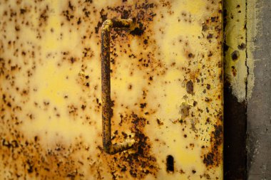 Paslı bir kapı kolu ve metal bir kapının üstündeki anahtar deliği endüstriyel bir bölgede pul pul boya ve oksitlenme gösteriyor..