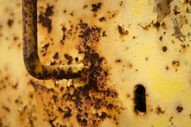 Paslı bir kapı kolu ve metal bir kapının üstündeki anahtar deliği endüstriyel bir bölgede pul pul boya ve oksitlenme gösteriyor..