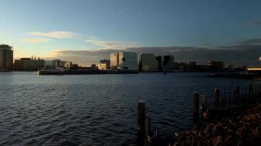 Amsterdam, Hollanda 'da günbatımında IJ nehrindeki modern binalarla Skyline. Döndürme çekimi.