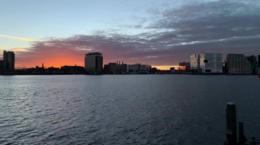 Amsterdam, Hollanda 'da günbatımında IJ nehrindeki modern binalarla Skyline. 