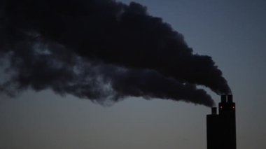 Endüstriyel bacalar alacakaranlıkta mavi gökyüzüne karşı duman yığınları.