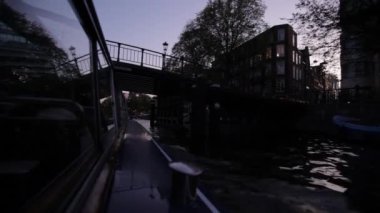 Hollanda, Amsterdam 'da alacakaranlıkta şehir kanalında bir tur teknesinden alçak görüş açısı.