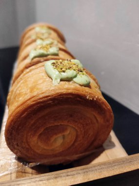 Cromboloni, New York Roll kruvasanı, üzerinde şam fıstığı sosu ile ahşap tezgahta servis edilir.