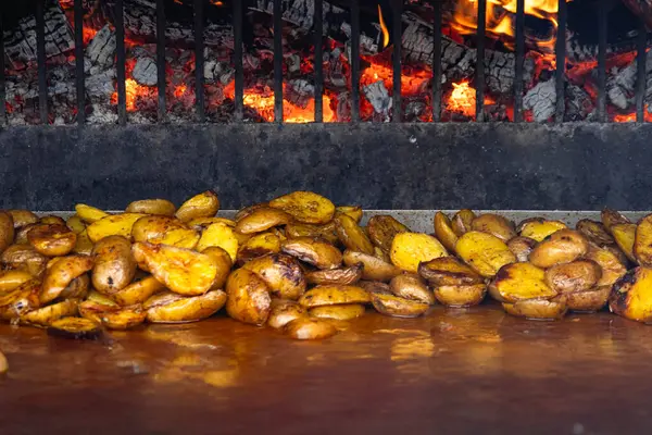 Canlı ateşi olan bir fırın. Patatesler açık ateşte pişirilir. Ahşap kütükler ateşte yanar. Patateslerin arka planında altın rengi var..