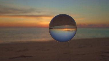 Güneş batarken deniz ve gökyüzünün doğal görüntüsü kristal kürenin içinde alışılmadık ve güzeldir. - Eşsiz ve yaratıcı bir yolculuk için bir görüntü. Güzel ve alışılmadık seyahat fikirleri için 4K Videolar.