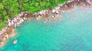 Hava manzaralı turkuaz deniz, kayanın yanında ve yamaçtaki yeşil orman. Adanın etrafını saran kayalar, turkuaz denize karşı. Phuket adasındaki kayalara yumuşak dalgalar çarpıyor. Kayaların dokusu arka planda.