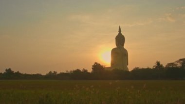 Muang Ang Thong Tayland 'da Tayland' ın büyük Buda 'sının önünde gün doğumu. Dünyanın en büyük Buda heykeli pirinç tarlalarıyla çevrili olarak uzaktan görülebilir..