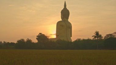 Muang Ang Thong Tayland 'da Tayland' ın büyük Buda 'sının önünde gün doğumu. Dünyanın en büyük Buda heykeli pirinç tarlalarıyla çevrili olarak uzaktan görülebilir..