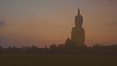 Muang Ang Thong Tayland 'da Tayland' ın büyük Buda 'sının önünde gün doğumu. Dünyanın en büyük Buda heykeli pirinç tarlalarıyla çevrili olarak uzaktan görülebilir..