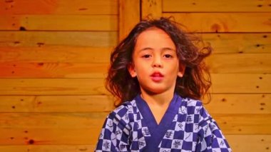 A cute little boy sits in a wooden room, swaying his hair.slow motion A little boy with long flowing hair sits in a wooden room.A happy atmosphere with a wooden backdrop.