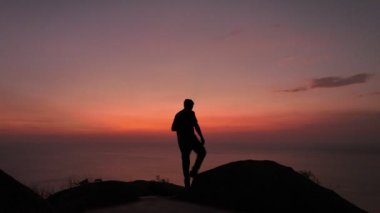 Kızıl gökyüzü ve deniz manzaralı bir sahneye karşı bir adam durur ve selfie çeker gökyüzünde ve deniz manzarası sarp kayalıklarda kırmızıdır alacakaranlık kırmızı gökyüzü..