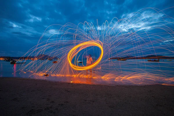 reflection of spark fire swirl from steel wool with long exposure speed motion abstract at sunrise in the sea.