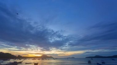 Güneş doğarken sarı gökyüzünde hareket eden hızlandırılmış bulutlar Rawai sahilindeki Phuket adalarının üzerinde yavaşça ilerliyorlar. Doğa videosu yüksek kaliteli görüntü. Renkli gökyüzü günbatımının bulut arkaplanlı sahnesi.