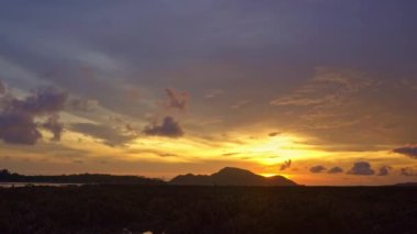 Güneş doğarken sarı gökyüzünde hareket eden bulutlar Rawai sahilindeki Phuket adalarının üzerinde yavaşça ilerliyorlar. Doğa videosu çok kaliteli. Mercan resifinin üzerinde sarı gün doğumu. Renkli gökyüzü arkaplanı manzarası.