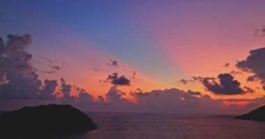 Tayland 'daki adanın üstündeki bulutların arasından geçen renkli pembe bir ışık.