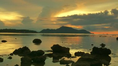 Güneş doğarken sarı gökyüzünde hareket eden bulutlar Rawai sahilindeki Phuket adalarının üzerinde yavaşça ilerliyorlar. Doğa videosu çok kaliteli. Mercan resifinin üzerinde sarı gün doğumu. Renkli gökyüzü arkaplanı manzarası.