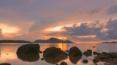 Deniz kenarındaki kayaların üzerinde gün doğumunda inanılmaz bir gökyüzü. Rawai plajı Phuket 'te sarı gün doğumu gökyüzünde bulutlar dolaşıyor. Deniz yüzeyinde gün doğumunun göz kamaştırıcı altın gökyüzü yansıması.  