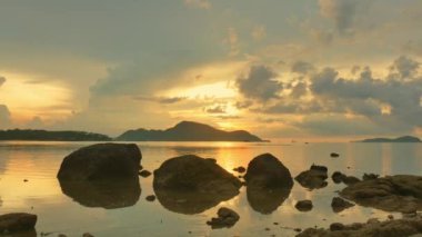 Güneş doğarken sarı gökyüzünde hareket eden bulutlar Rawai sahilindeki Phuket adalarının üzerinde yavaşça ilerliyorlar. Doğa videosu çok kaliteli. Mercan resifinin üzerinde sarı gün doğumu. Renkli gökyüzü arkaplanı manzarası.