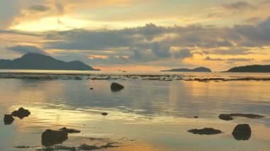 Güneş doğarken sarı gökyüzünde hareket eden bulutlar Rawai sahilindeki Phuket adalarının üzerinde yavaşça ilerliyorlar. Doğa videosu çok kaliteli. Mercan resifinin üzerinde sarı gün doğumu. Renkli gökyüzü arkaplanı manzarası.
