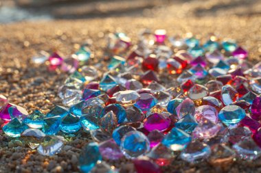 Kumsala saçılmış renkli elmaslar. Değerli taşların yüzeyinde güneş parlıyordu.
