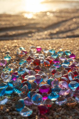 Kumsala saçılmış renkli elmaslar. Değerli taşların yüzeyinde güneş parlıyordu.