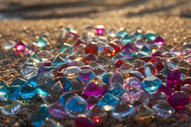 Kumsala saçılmış renkli elmaslar. Değerli taşların yüzeyinde güneş parlıyordu.