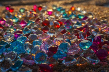 Kumsala saçılmış renkli elmaslar. Değerli taşların yüzeyinde güneş parlıyordu.