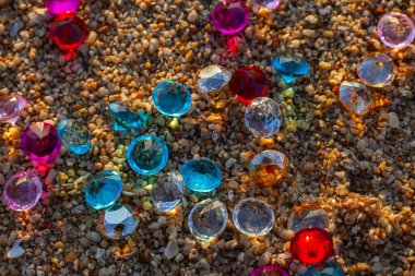 Kumsala saçılmış renkli elmaslar. Değerli taşların yüzeyinde güneş parlıyordu.