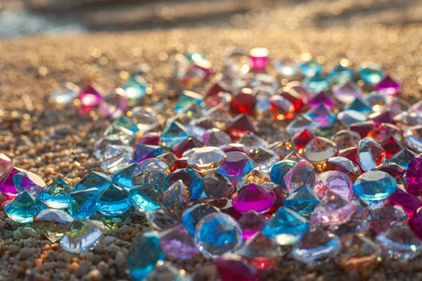 Kumsala saçılmış renkli elmaslar. Değerli taşların yüzeyinde güneş parlıyordu.