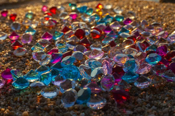 Kumsala saçılmış renkli elmaslar. Değerli taşların yüzeyinde güneş parlıyordu.