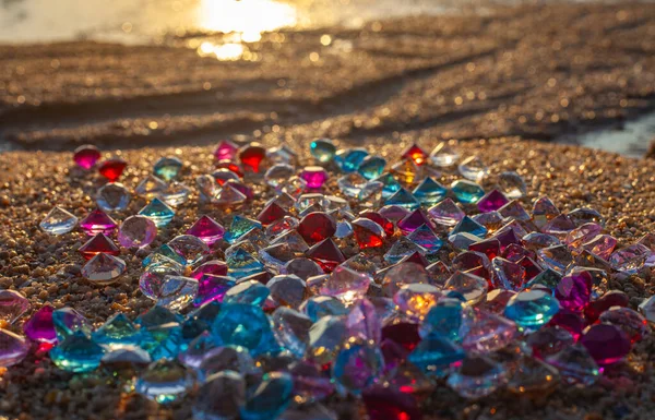 Kumsala saçılmış renkli elmaslar. Değerli taşların yüzeyinde güneş parlıyordu.