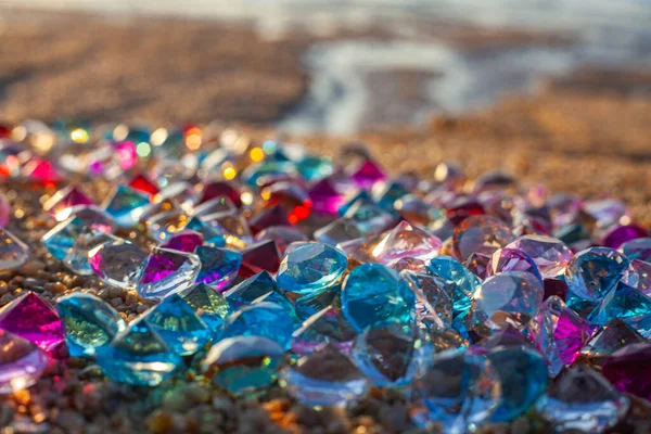 Kumsala saçılmış renkli elmaslar. Değerli taşların yüzeyinde güneş parlıyordu.