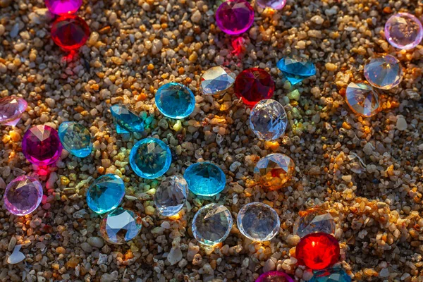 Kumsala saçılmış renkli elmaslar. Değerli taşların yüzeyinde güneş parlıyordu.