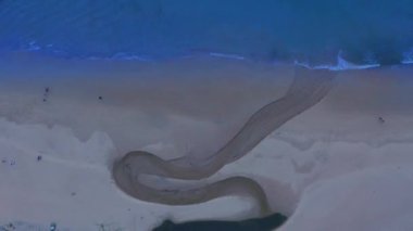 Kumsaldaki dolambaçlı kanal havadan görülebilir. Göletteki su, denize doğru akar.